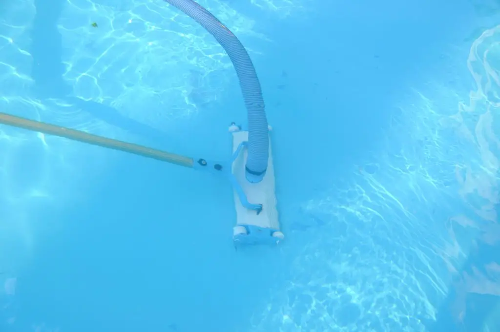 a manual pool vacuum at the bottom of a pool cleaning debris
