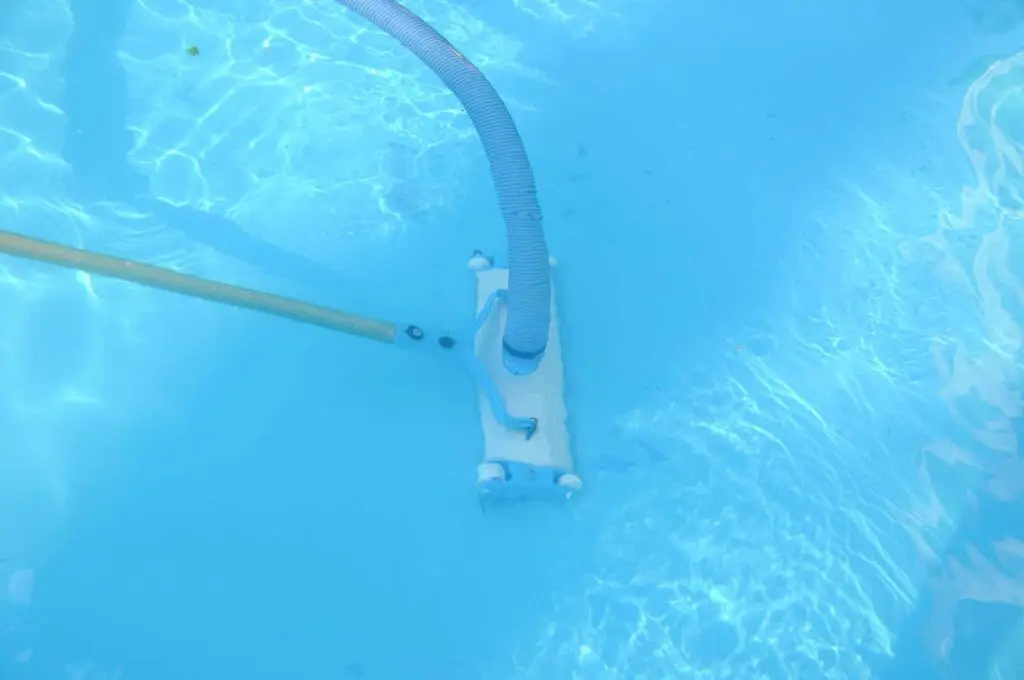 a manual pool vacuum at the bottom of a pool cleaning debris